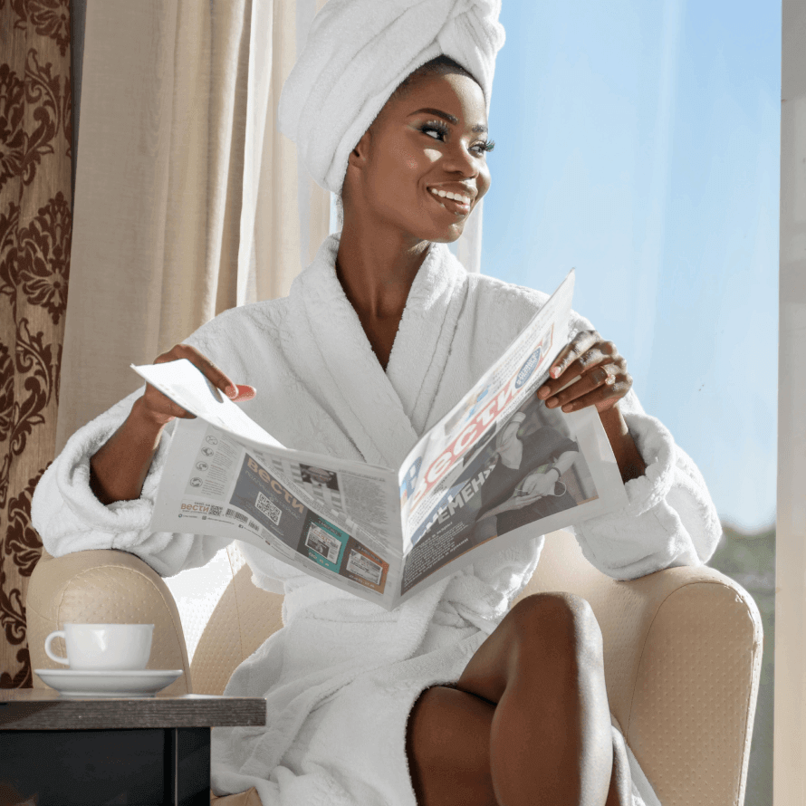 Woman in a robe reading about Korean cosmetics effectiveness while enjoying coffee by the window